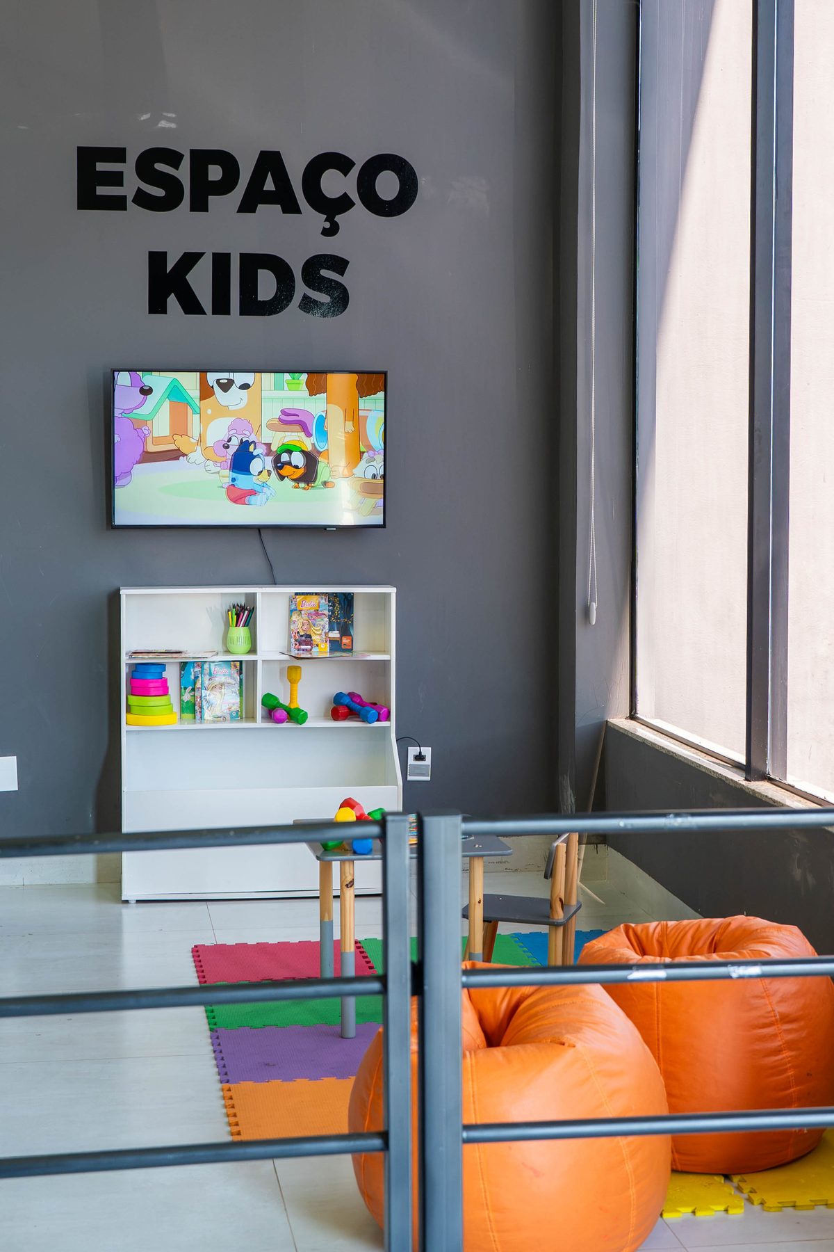 Espaço Kids da Sparta Gym, com tatame, brinquedos, puffs e TV
